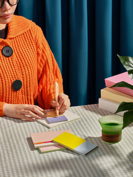 A person writes on a colorful notepad, wearing an orange sweater