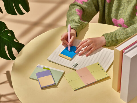 A hand writes on a sticky note atop a notebook at desk