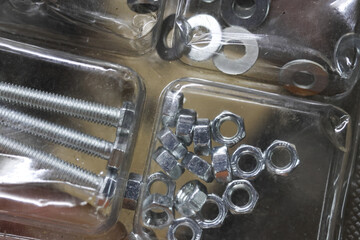 Close up view of hardware collection with shiny metal screw, nut, and washer in plastic tray. An assortment of fasteners creating useful background for assembly work