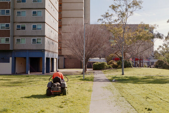 Lawn Mower Operator Maintains Green Space Near Urban Buildings