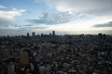 A panoramic view of Tokyo’s urban skyline at sunset, featuring dramatic clouds and a mix of modern skyscrapers and dense city streets.