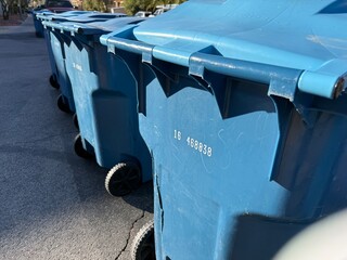Curbside Recycling Bins: Row of blue plastic trash bins lined up on a street curb for collection.