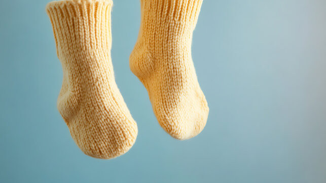 Two knitted yellow socks, soft texture, suspended against a calming blue backdrop. Simple cozy comfort, showcasing delicate knitwork in soft light.