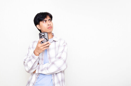 Young man looking confused while checking his smartphone, expressing doubt and decision-making in a digital context on a clean white background.