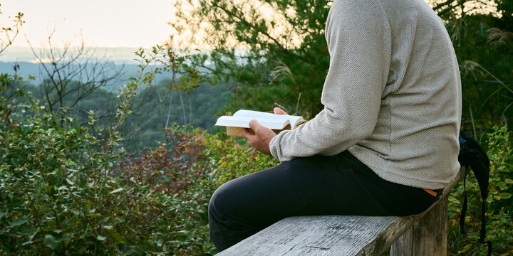 山のベンチで本を読む男性