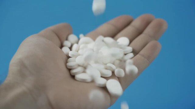 White pills and tablets falling into a person's open hand for medical treatment and health care