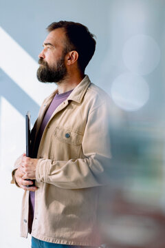 Professional Bearded Man In Beige Jacket Holding a Laptop