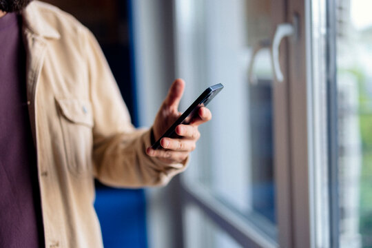 Casual Man in Beige Jacket Using Smartphone by Window