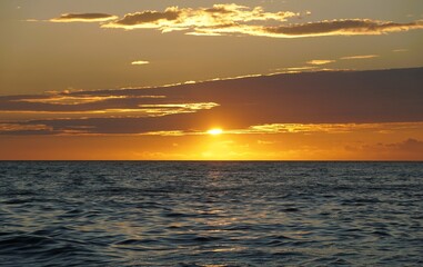 Sunset over ocean creates warm light reflections and layered clouds, signaling end of day and stable weather conditions near Madeira Beach, Florida, U.S.A
