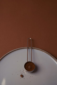 Freshly ground coffee in a measuring spoon on a simple white plate 