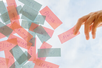 pink and blue pieces of paper with male and female names against a sky