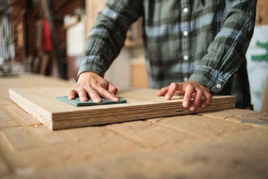 Hands Sanding Wooden Board on Workbench