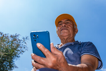 Mexican elderly man using mobile phone outdoors under blue sky