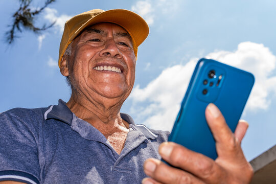 Elderly mexican man smiling using smartphone outdoors