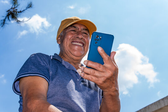 Mexican senior man smiling using phone outdoors