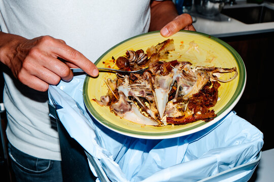 a man scrapes chicken bones and snails into a trash bin