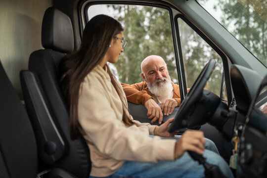 Father giving driving instructions to young woman in campervan