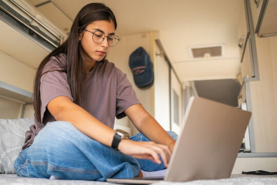 Young woman using laptop lying in campervan bed