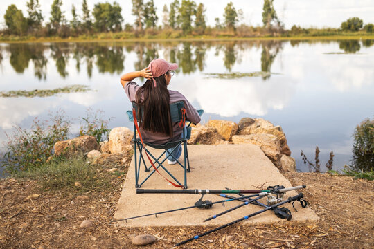 Young woman sitting by the river with fishing rods