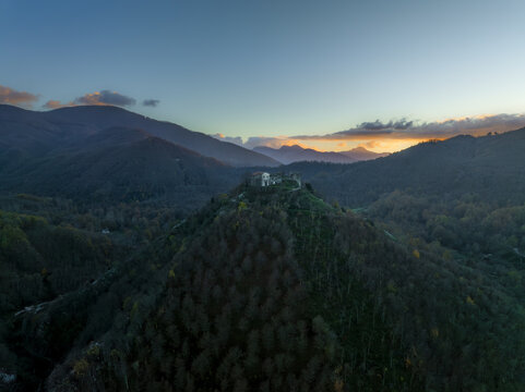 Aerial view of a striking white building perched atop a lush, tree-covered hill at dusk, contrasting against the deep blue sky, Volturara Irpina, Campania, Italy.