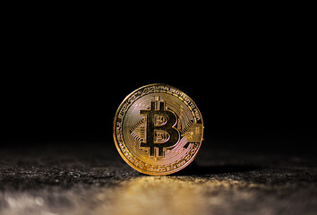 Single Gold Bitcoin Coin Standing on Dark Textured Surface Shiny Bitcoin Token Illuminated Against Black Background