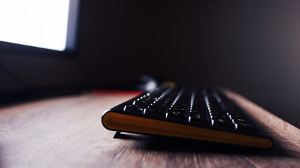 Wireless Keyboard on Wooden Desk Near Monitor Light  Side View of Modern Keyboard in Dim Workspace Lighting