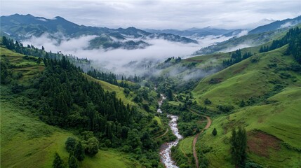 Obraz premium Aerial view of a lush valley with a meandering river, surrounded by rolling hills and mountains shrouded in mist