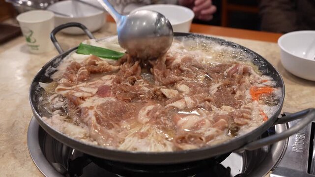 Serving Korean Bulgogi Hot Pot with Shabu-shabu Style Meat, Vegetables, and Broth, Stirring Thinly Sliced Pork and Noodles in Savory Soup, Fresh Meat Boiling in Stew