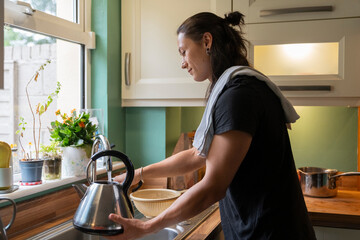 Young Man Fills Electric Kettle With Water in Kitchen for Cooking