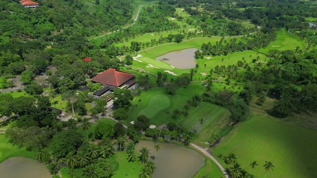 A downward tilt up wide shot of Canlubang Golf and Country Club showing fairways, water features, tropical trees, and cloud shadows in Calamba Laguna, Philippines