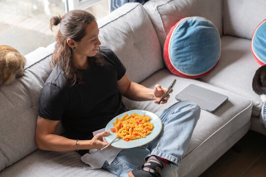 Man Enjoying Pasta Meal While Relaxing on Couch and Using Phone