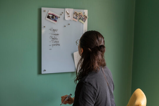 Man Writes Groceries List on Glass Board in Kitchen With Green Wall