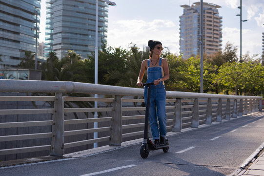 Woman rides electric scooter on bridge in city.