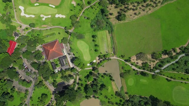 A higher top view aerial showcasing the expansive grounds of Canlubang Golf and Country Club, revealing manicured fairways, brown puddles, and tropical greenery in Calamba Laguna, Philippines