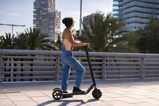 Woman on scooter in city, palm trees and buildings.