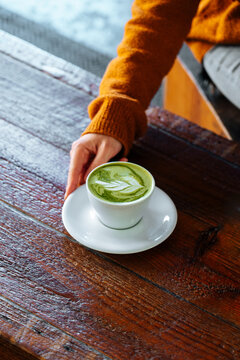 Hand reaching for matcha latte on wooden table