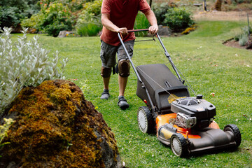 Man mowing a lawn with a lawn mower in a sunny garden