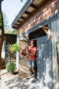Friendly farmer in shed holding chicken outdoors, smiling
