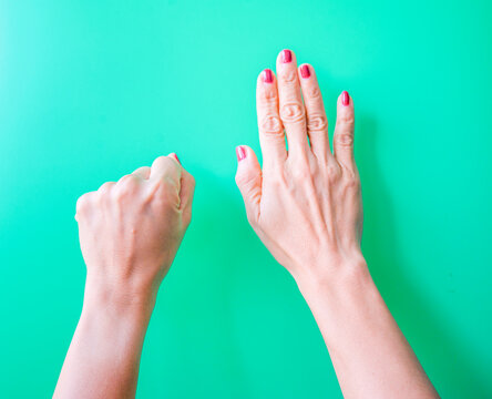 Female hands with manicure on a green background, top view.