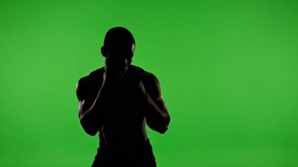 Silhouette of a muscular boxer training in a dark studio against a green screen showcasing intense shadow boxing and fitness workout for sports and healthrelated content. - Powered by Adobe