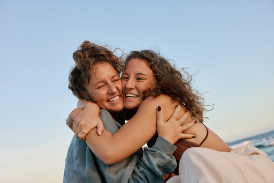 Playful Twin Sisters Hug on Beach