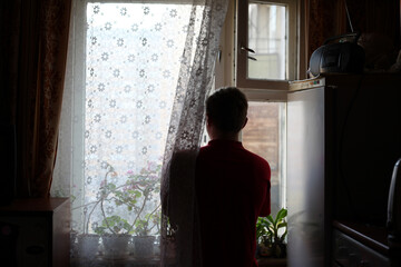 Person standing by window with lace curtain and plants