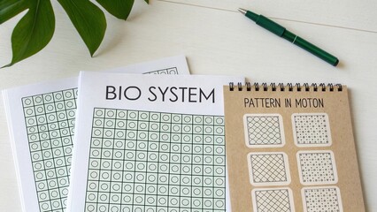 Creative workspace with bio system charts and pattern in motion notebook on wooden desk with green plant and pen