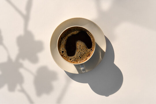 Black Coffee with Foam in a Ceramic Cup and Saucer under Sunlight.