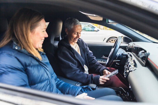 Two Women Smiling and Using Smartphone in Modern Car