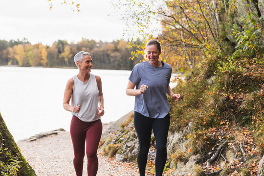 Happy Friends Jogging Together on Lakeside Trail in Autumn