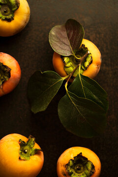 Ripe persimmons with fresh leaves on dark surface