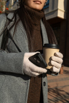 Woman holding coffee and phone in winter urban setting