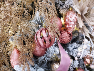 Close-up, abstract, and blurry photo of a lavish Christmas decoration display. The image features a mix of metallic textures, dominated by rose gold and dull pink. Christmas tree blurred background.