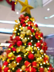 a deliberately blurred photo (bokeh effect) of a large, brightly decorated Christmas tree, draped in twinkling yellow-white lights that form a glowing circle (bokeh)